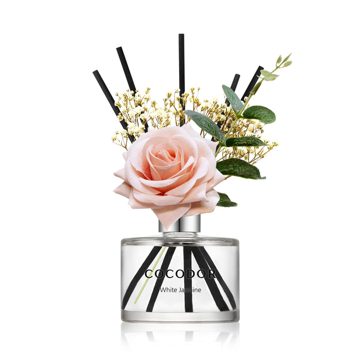 a bottle of fragrance with a pink rose and black sticks