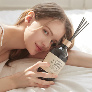 a woman lying on a bed holding a bottle of perfume