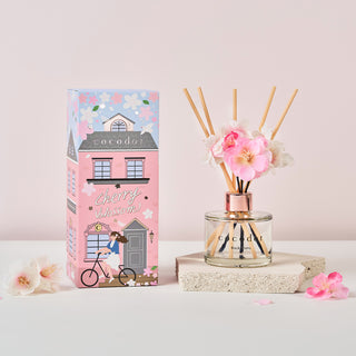 a pink and white box next to a glass bottle with flowers